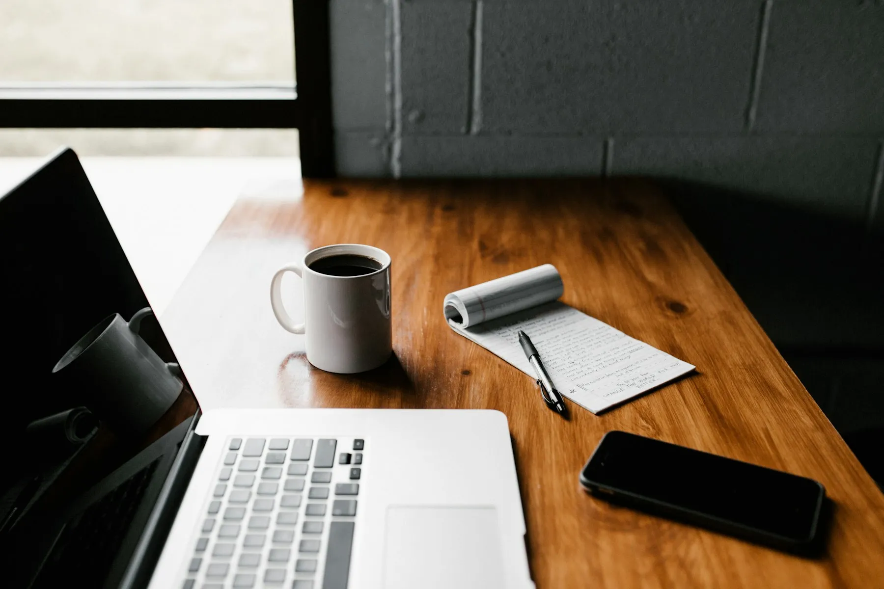 Laptop, catatan, dan kopi di atas meja kayu